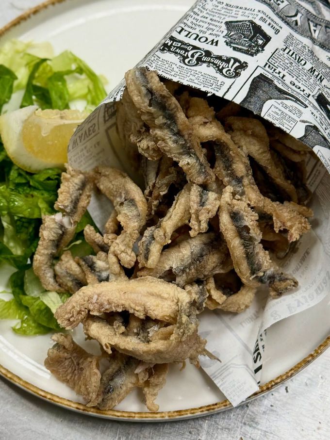 Pesce fritto in un cono di carta con lattuga e limone su un piatto.