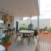 Modern patio with round dining table, black chairs, wood deck, potted plants, and hanging egg chair