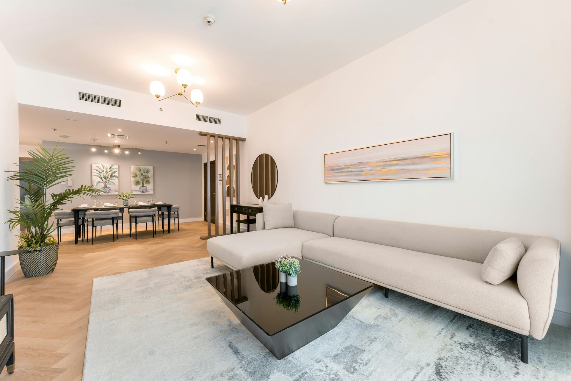 Bright living room with a beige sectional, glass coffee table, and dining area in the background