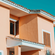 Sunlit peach stucco house facade with white trim and shuttered windows under a tiled roof