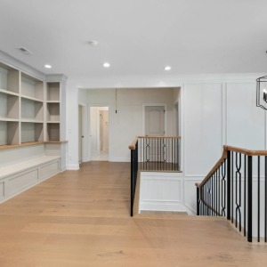 Bright upstairs hallway with built-in white shelves, light wood floors, and stair railings overlooking a foyer