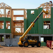 Yellow crane lifting materials at a building under construction with green wall panels and wood framing.