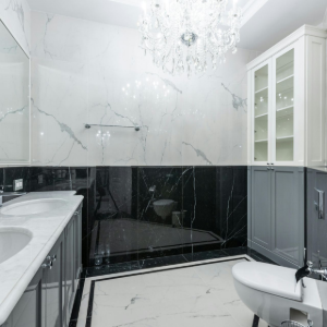 Elegant black-and-white bathroom with marble tile, chandelier, vanity, bathtub, and toilet