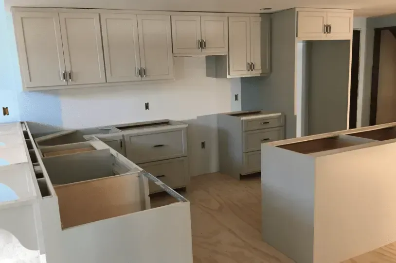Unfinished kitchen with white cabinets, gray island, and exposed countertops under renovation