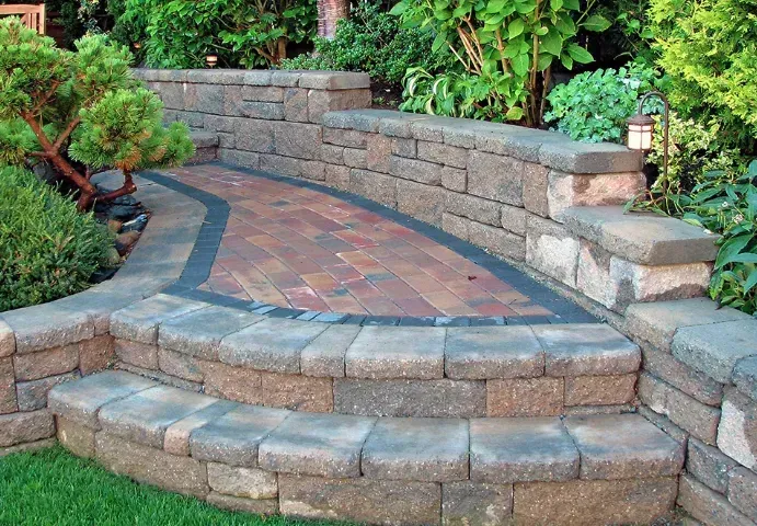 Curved stone garden steps with a brick landing and retaining wall, surrounded by lush greenery