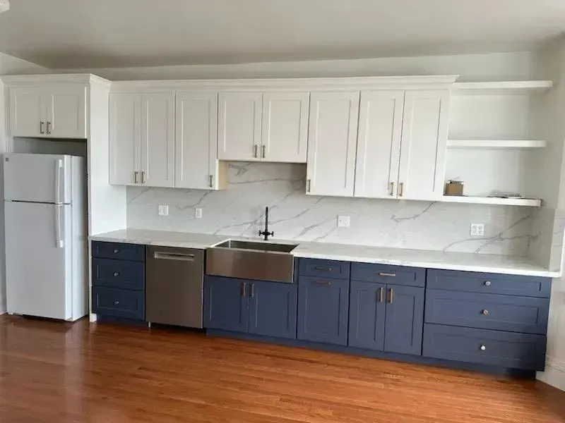 Modern kitchen with white upper cabinets, navy lower cabinets, stainless appliances, and hardwood floors.