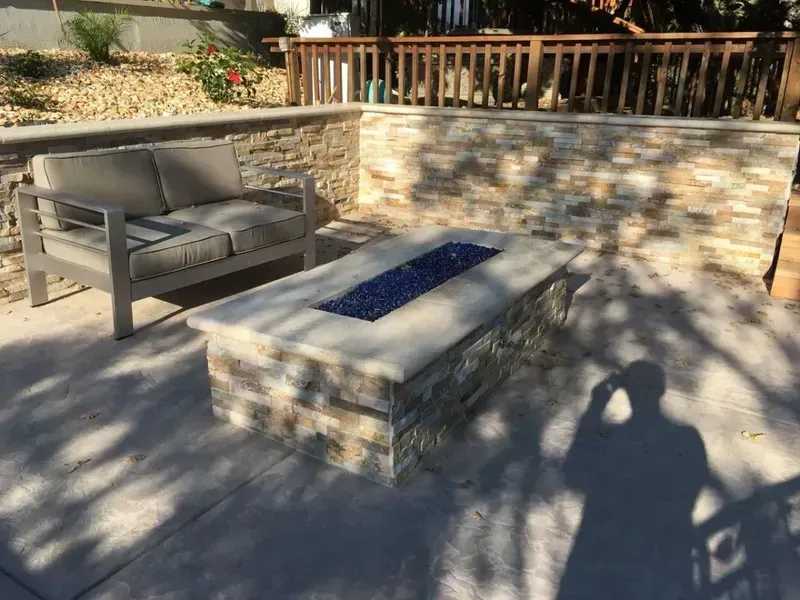Outdoor patio with gray chair, stone fire pit, and sunlit retaining wall