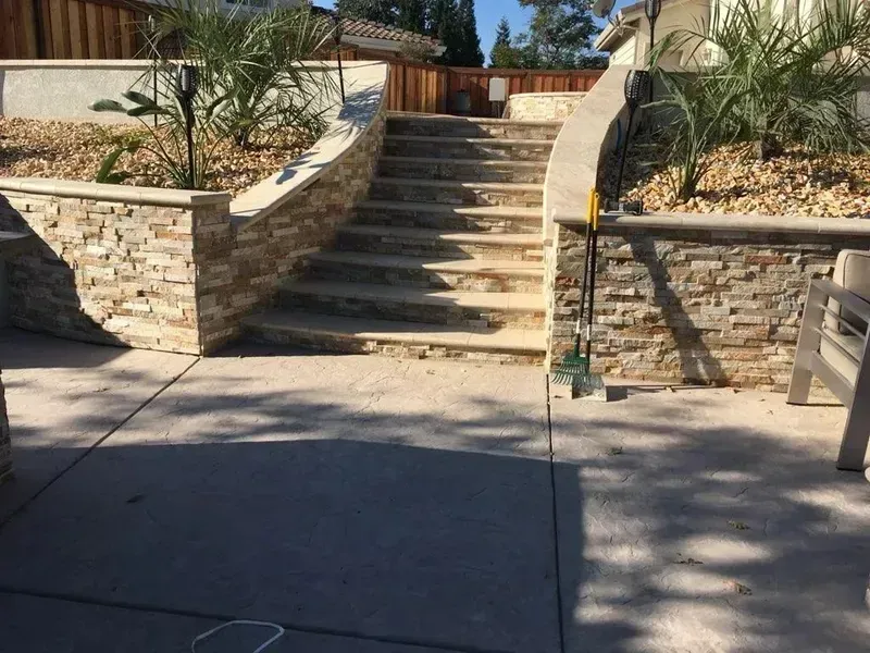 Stone steps leading to a gated entrance between low stone walls in a sunny courtyard