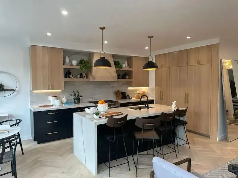 Modern kitchen with white island, black stools, wood cabinetry, and pendant lights