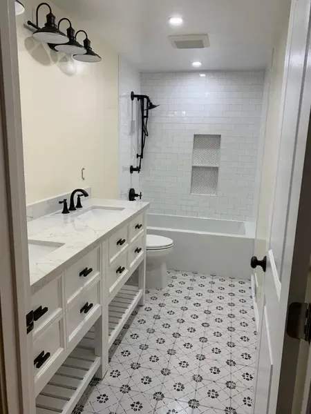 Bright bathroom with white vanity, patterned tile floor, toilet, and bathtub/shower alcove