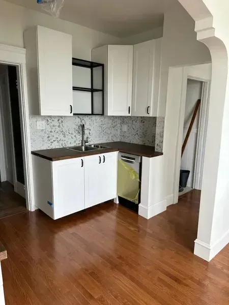 Small kitchen nook with white cabinets, dark counters, mosaic backsplash, and wood floors.