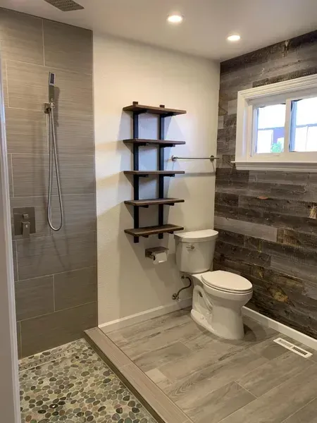 Modern bathroom with walk-in shower, toilet, wood shelving, and window over rustic tile wall