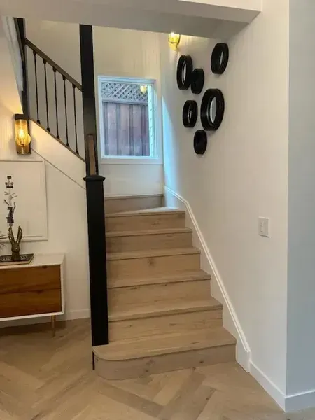 Narrow staircase in a bright hallway with beige steps, black railing, and wall decor