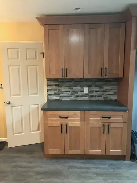 Built-in wooden cabinets with tile backsplash beside a white door in a kitchen nook