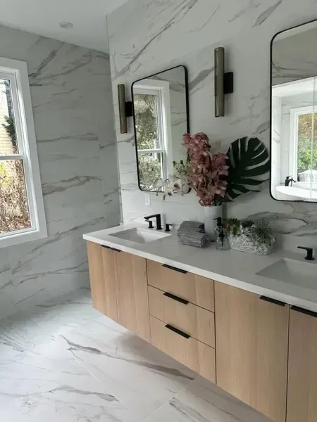 Modern bathroom with marble walls and floors, wood vanity, black fixtures, and a large mirror.