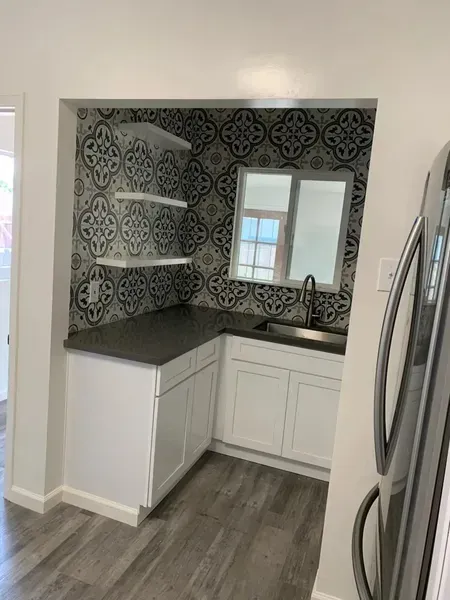 Small kitchen nook with white cabinets, black countertop, patterned tile backsplash, and open shelves.