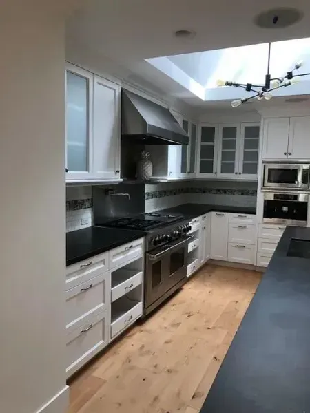 Modern kitchen with white cabinets, stainless steel appliances, black countertops, and light wood floors