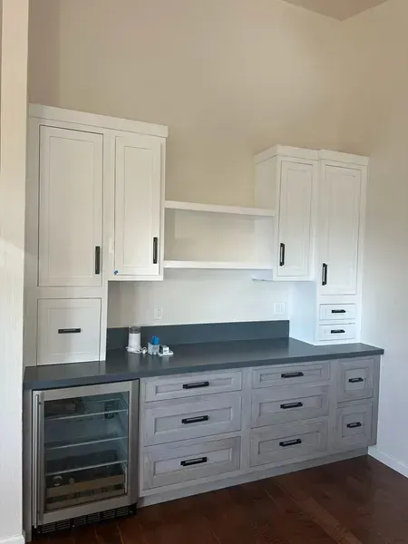 Built-in gray and white kitchen cabinets with dark countertop and open shelf.