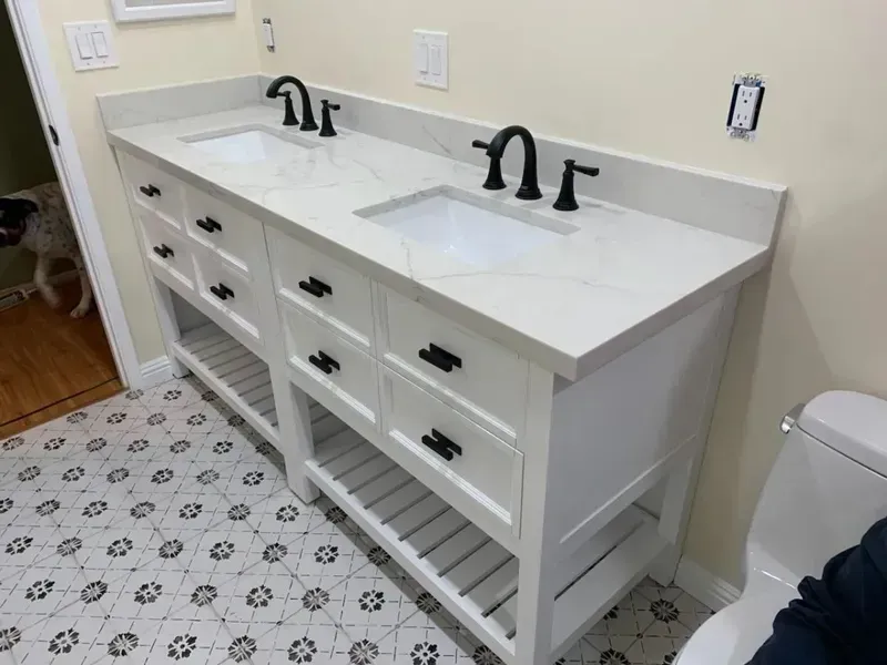 White double vanity with black faucets, drawers, and open shelves in a bathroom with patterned tile floor.