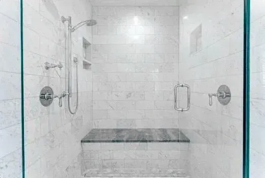 Glass-enclosed white tiled shower with chrome fixtures and a built-in bench.