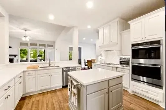 Bright white modern kitchen with island, wood floors, and built-in double ovens