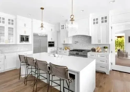Bright white modern kitchen with island, bar stools, stainless appliances, and wood floors