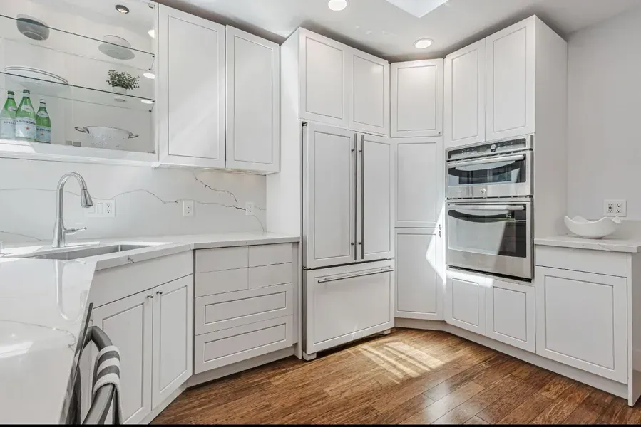 Bright white modern kitchen with stainless steel appliances, wood floor, and glass-front cabinets