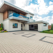 Modern two-story house with a large paved driveway and glass balcony under a partly cloudy sky