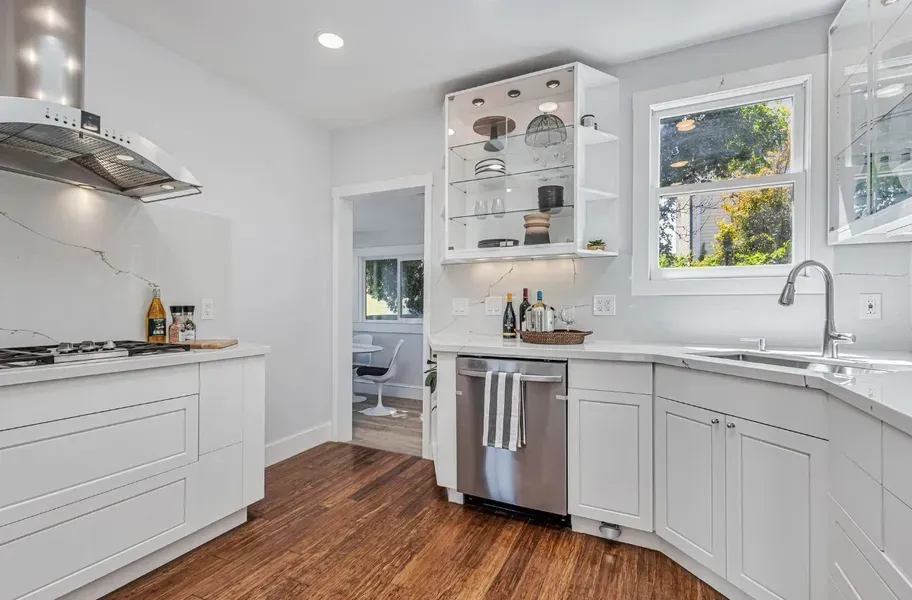 Bright modern kitchen with white cabinets, stainless appliances, wood floors, and a window over the sink