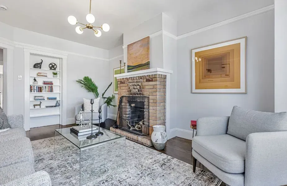 Bright living room with a stone fireplace, gray chair, glass coffee table, and white built-in shelves.