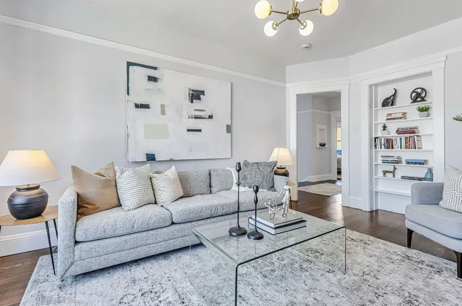 Bright modern living room with a gray sofa, patterned rug, coffee table, and white built-in shelves.