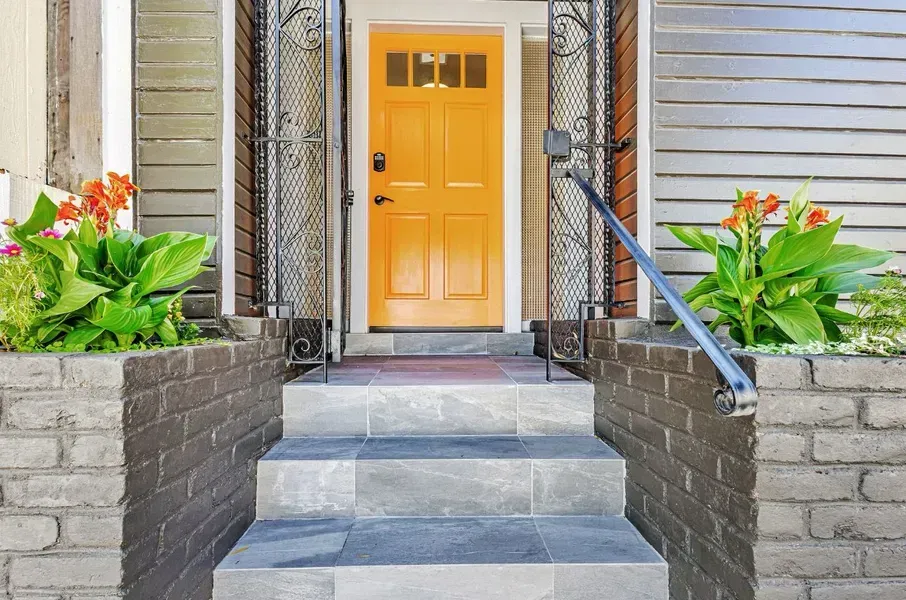 Front porch with yellow door, gray steps, black railings, and flower planters on both sides