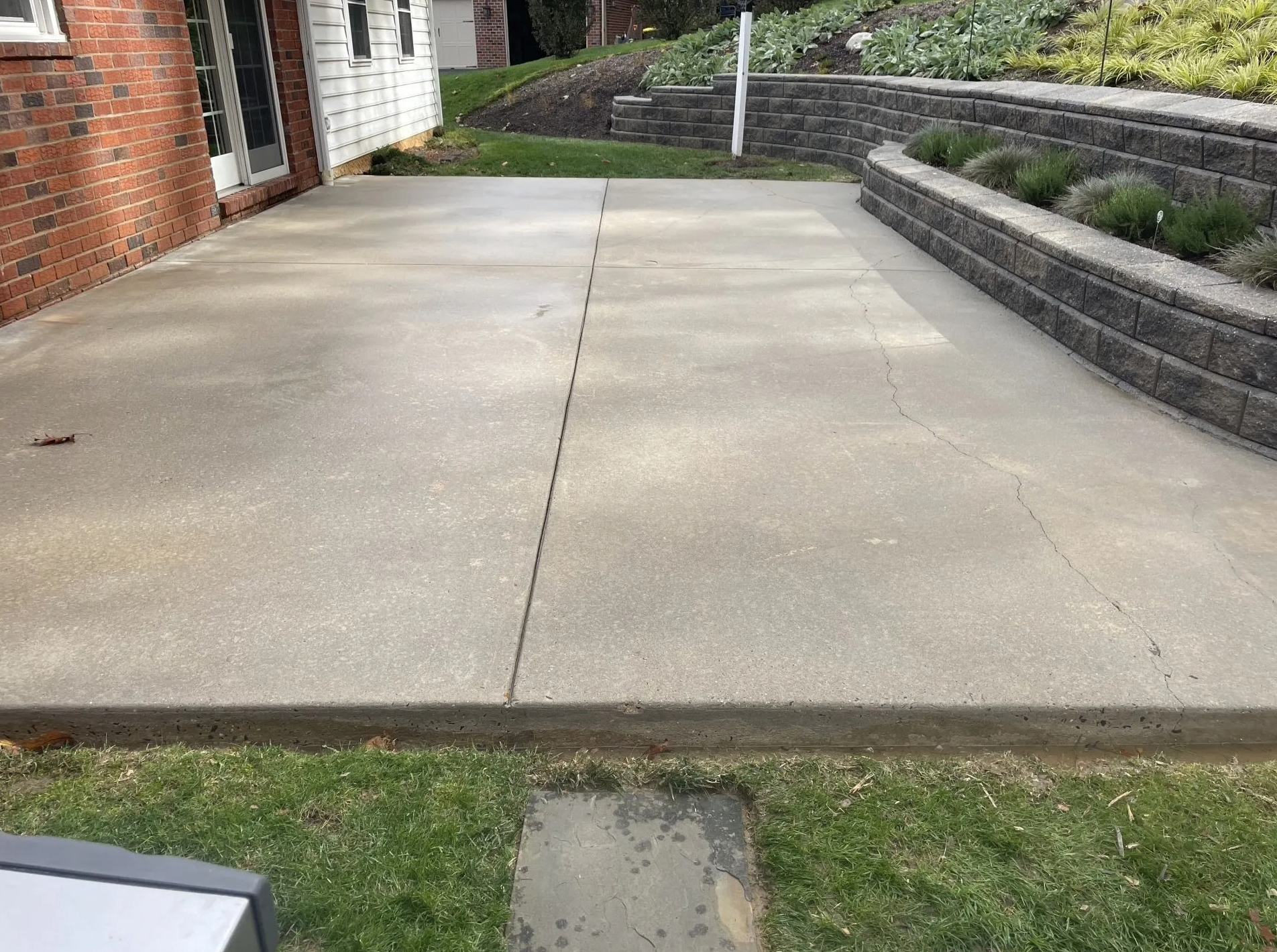 Concrete patio with cracks next to a brick building and a tiered retaining wall.
