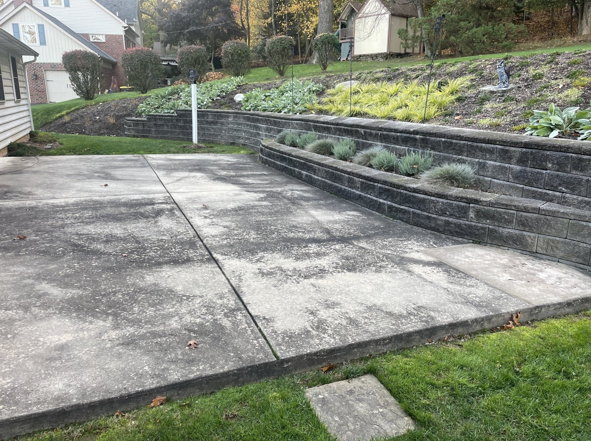 Concrete patio with tiered retaining walls of plants and grass, under cloudy skies.