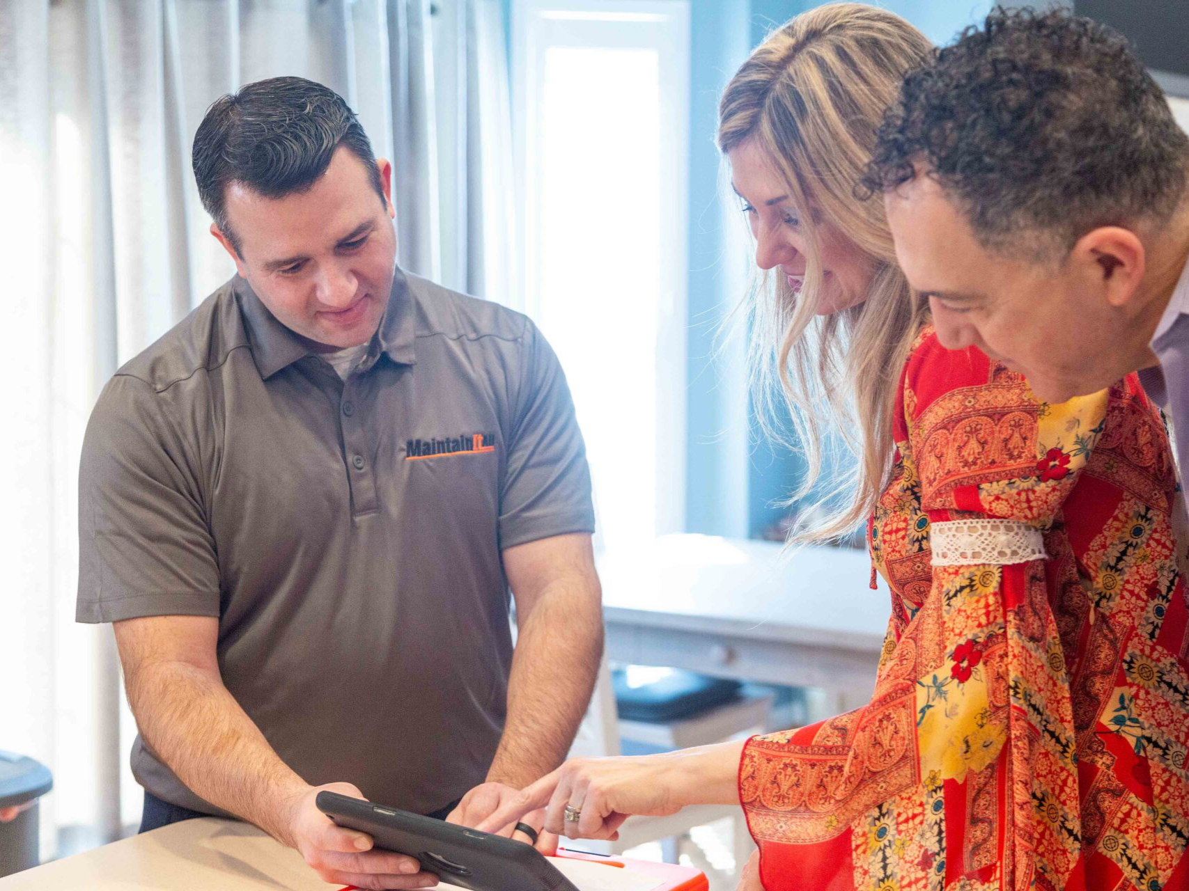 Man in gray shirt showing tablet to a couple; they are looking at it and smiling. Indoors.