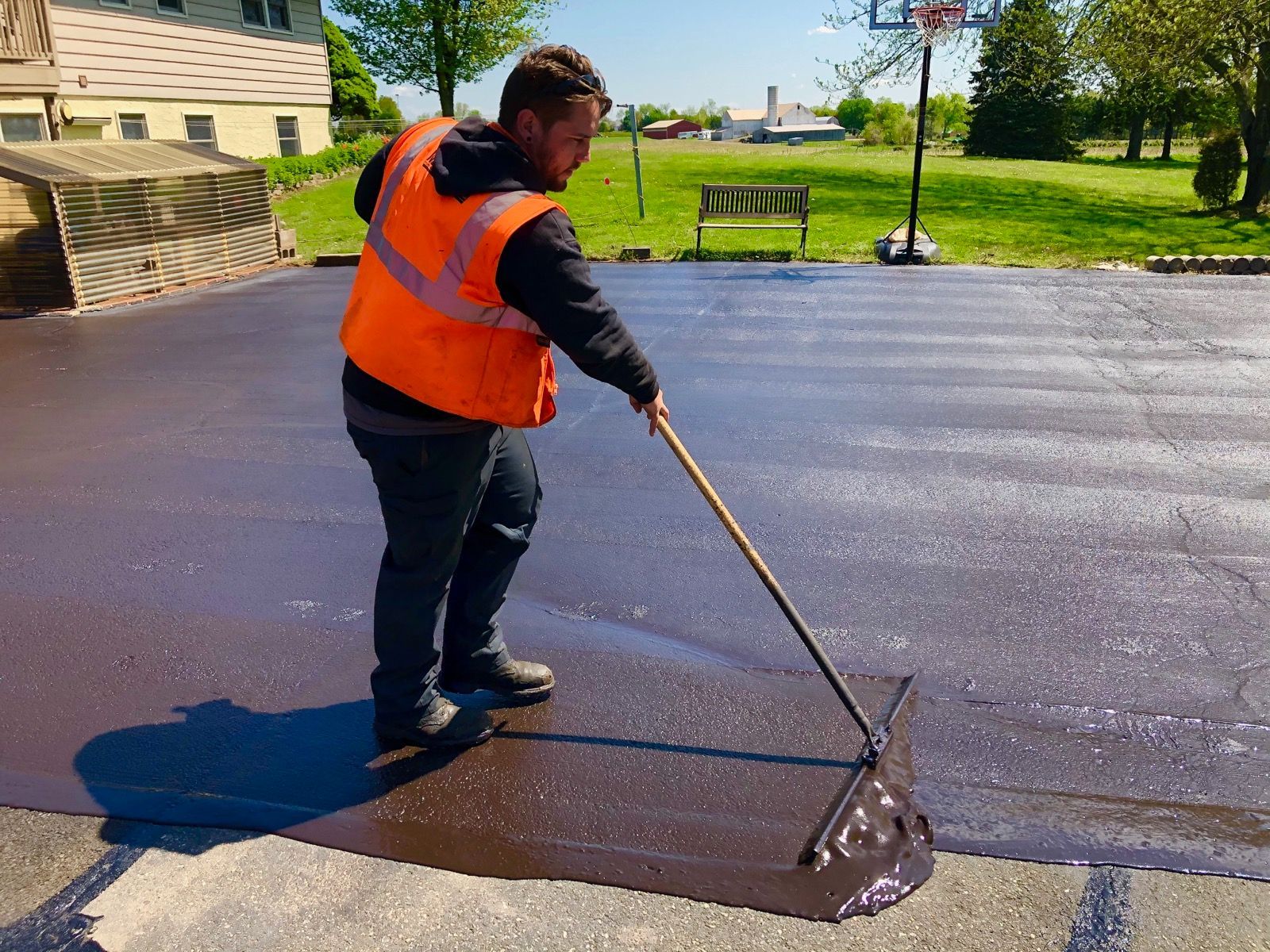 Worker in orange safety vest spreading fresh asphalt with a rake on a paved road