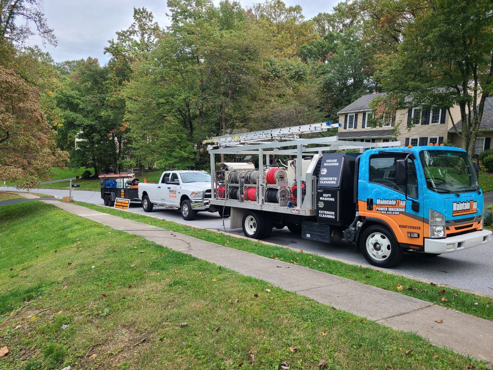 A service truck with blue and orange branding and a trailer parked on a suburban street near trees and houses.