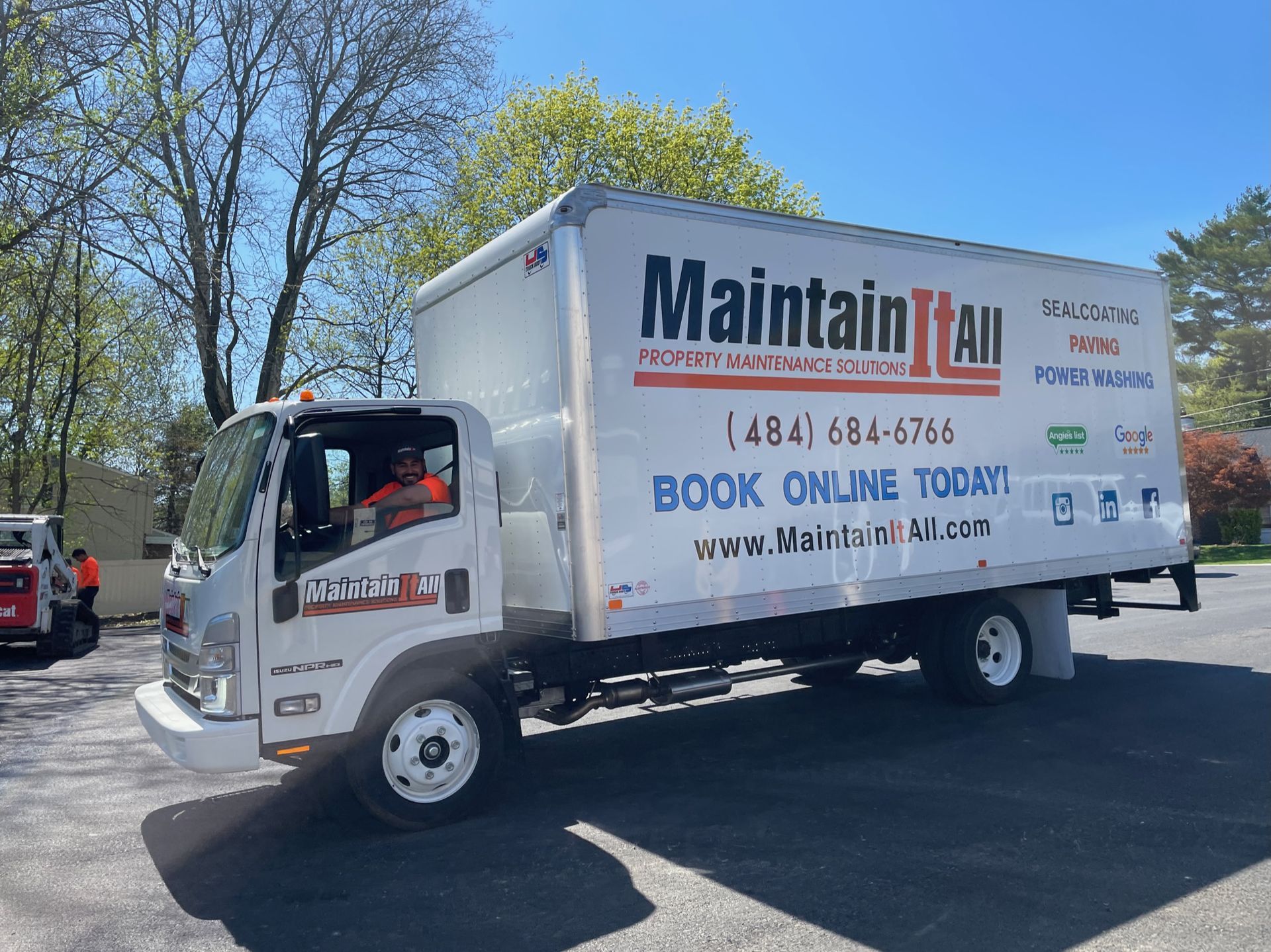 A white MaintainItAll box truck parked outdoors on a sunny day with a driver inside.