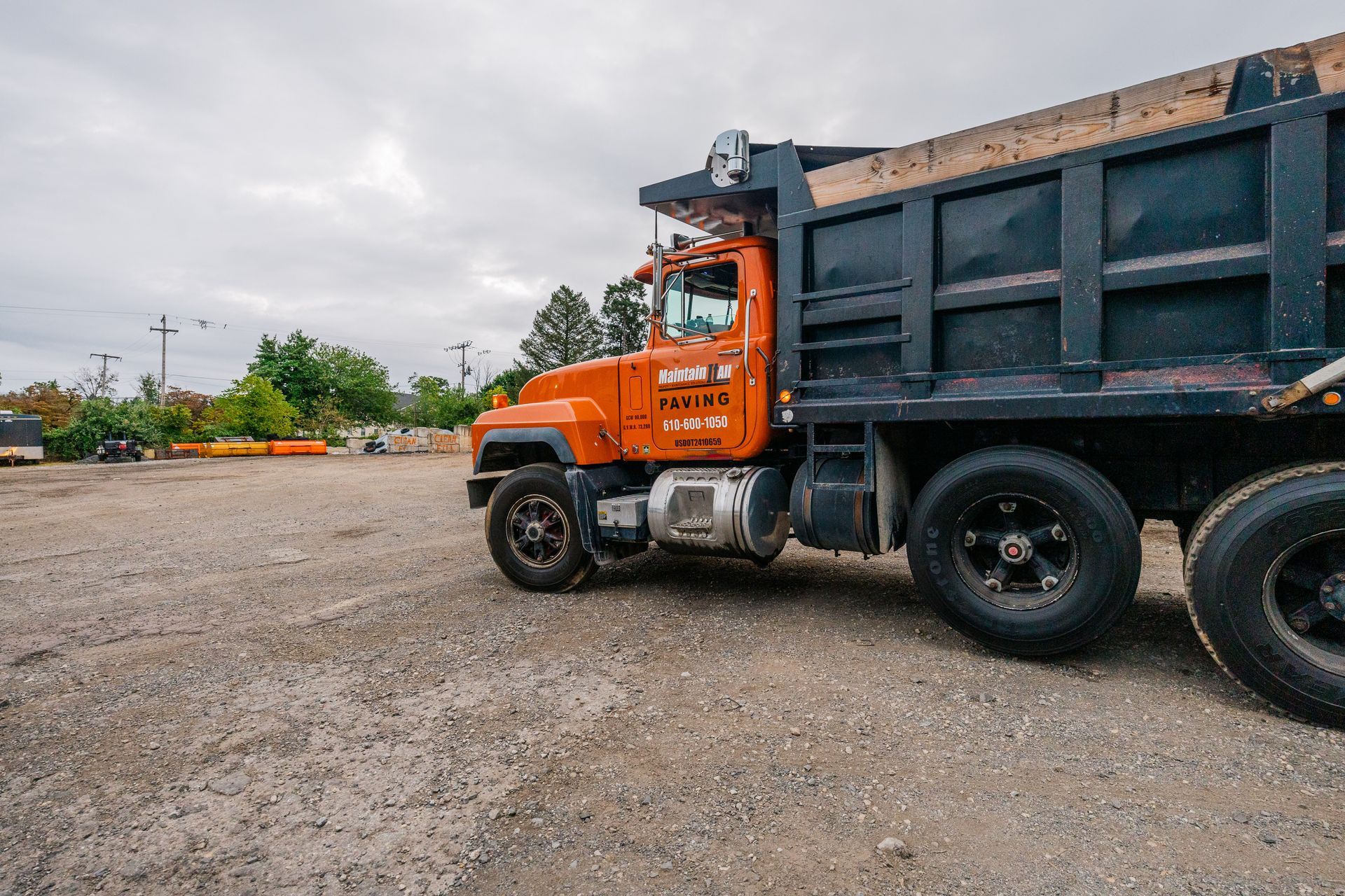 Orange dump truck parked on a gravel lot under a cloudy sky