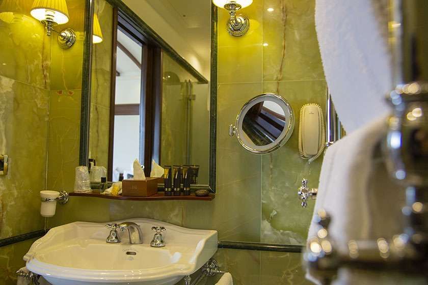 A white sink in a bathroom with green marble walls, a mirror, a magnifying wall mirror, and a wall-mounted telephone.