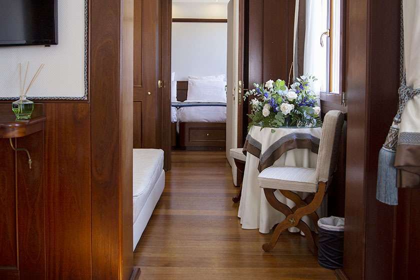 A view looking through a wood-paneled hallway into a bedroom with a draped side table, flowers, and a small chair.
