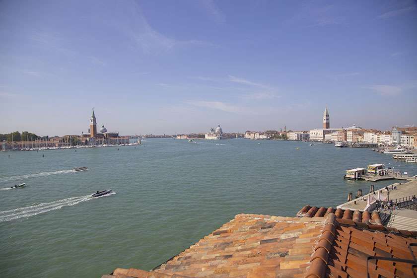 A wide-angle view of the Venetian lagoon, showing the city skyline with church towers and boats on the water.