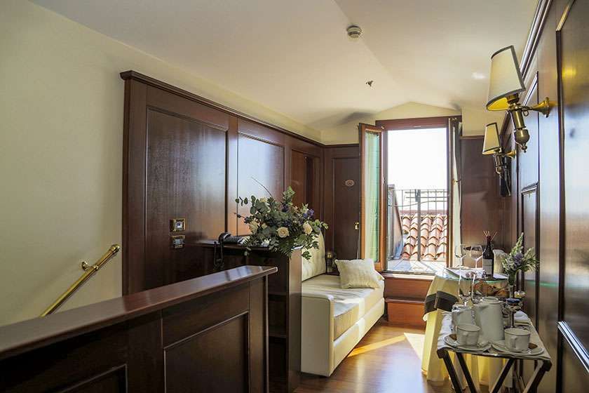 A cozy hotel hallway with wood-paneled walls, a small sofa, a window overlooking a tiled roof, and a room service table.