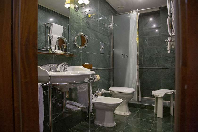 A bathroom with dark green marble walls featuring a pedestal sink, a bidet, a toilet, and a walk-in shower.