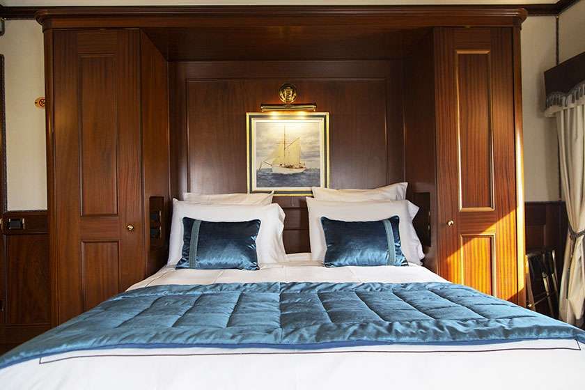 A bed with a blue quilted cover and matching pillows, framed by dark wood cabinets with a nautical painting above.