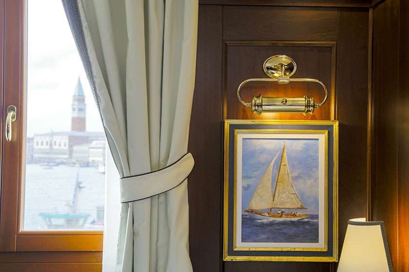 A window overlooking the Venice skyline next to a wall featuring a framed sailboat painting and a brass picture light.