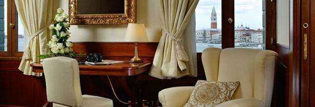 A plush armchair and desk in a classic hotel room, overlooking a view of Venice, Italy.