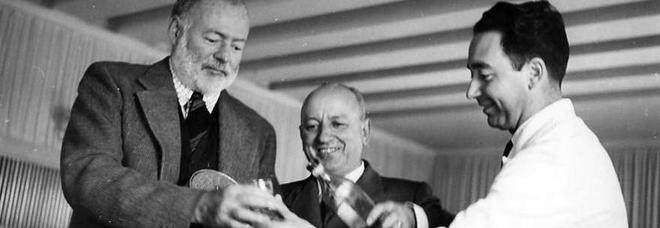 Ernest Hemingway, Alfred Hitchcock, and another man smiling while holding glasses in an indoor setting.