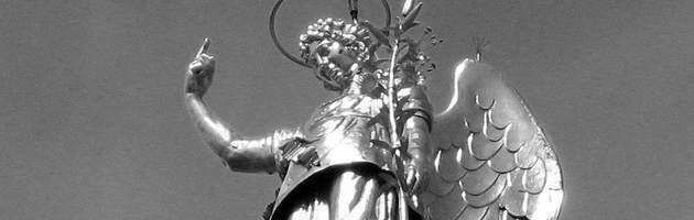 A gold-toned statue of a winged angel with a halo, pointing a finger upward and holding a palm frond against a grey sky.