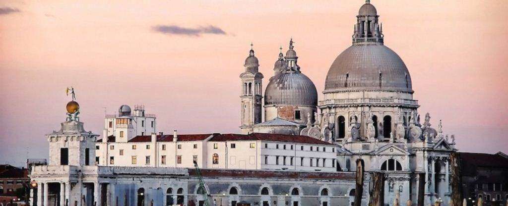 Santa Maria della Salute cathedral in Venice, Italy, at sunset with a soft pink sky backdrop.